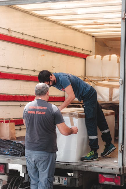 A professional removal service at a residential property featuring two individuals involved in a home relocation process. A male removal worker with dark curly hair, a beard, and wearing a dark blue u
